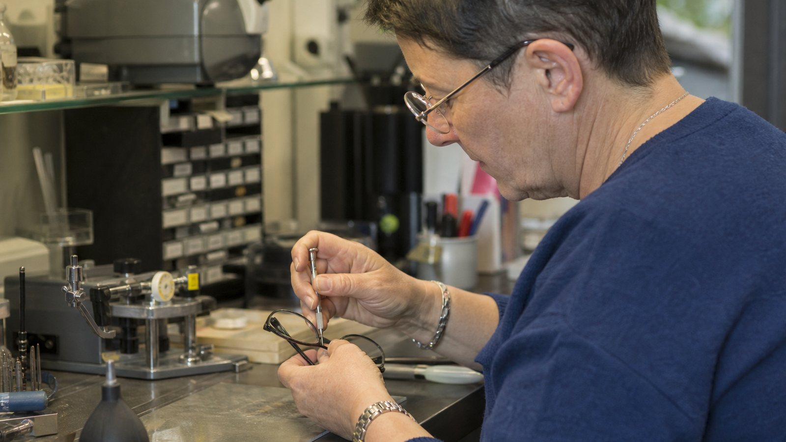 Opticien réparant une paire de lunettes à l'établi de son atelier, outils à portée de main